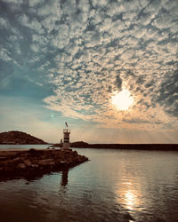 Lighthouse by sea against sky during sunset