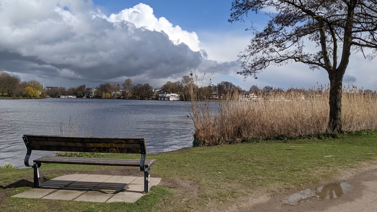 EMPTY BENCH BY LAKE AGAINST SKY DURING SUNNY DAY