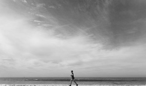 Man running at beach against sky