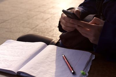 Midsection of person using mobile phone with notebook on street