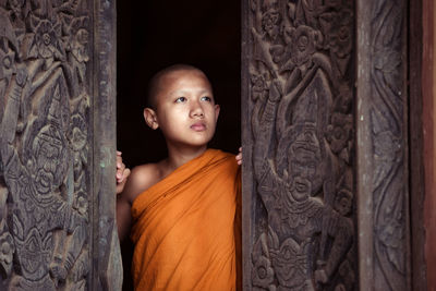 Boy monk looking away while standing at doorway