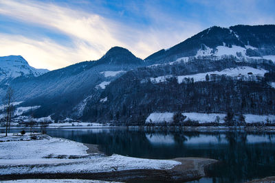 Scenic view of lake by snowcapped mountains against sky