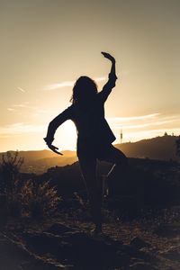 Rear view of silhouette young woman exercising on field against sky during sunset