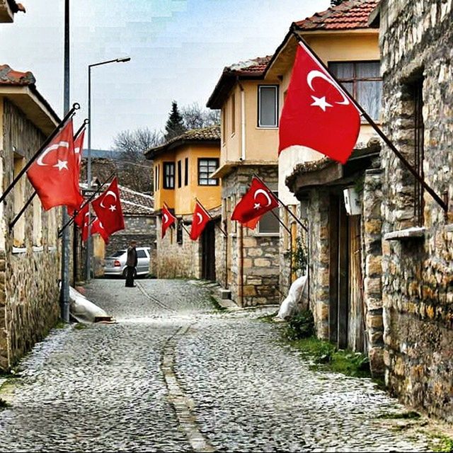 architecture, building exterior, built structure, red, the way forward, flag, patriotism, cobblestone, house, national flag, street, day, lantern, footpath, identity, walkway, sky, residential structure, outdoors, pathway