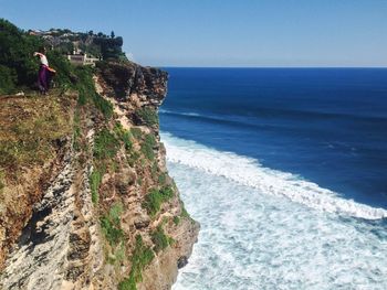 Woman standing on cliff by sea against clear sky