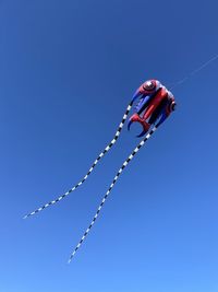 Low angle view of kites flying against clear blue sky