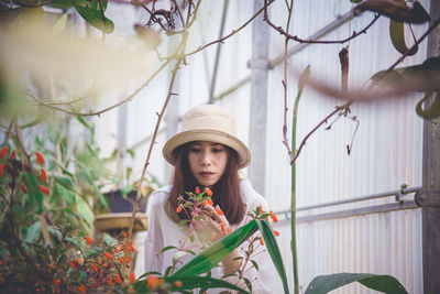 Woman wearing hat touching flowering plant