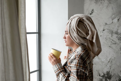 Young woman with towel on her head drinking coffee