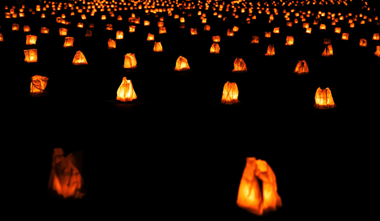 lighting equipment, illuminated, font, lantern, large group of objects, celebration, tradition, candle, orange color, night, no people, darkness, fire, burning, glowing, flame, in a row, black background, traditional festival, lighting, nature, event, religion, dark, indoors