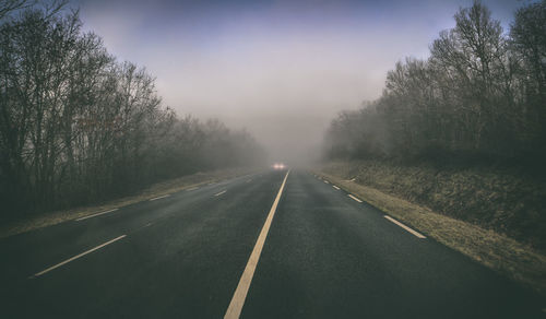 Empty road amidst trees against sky