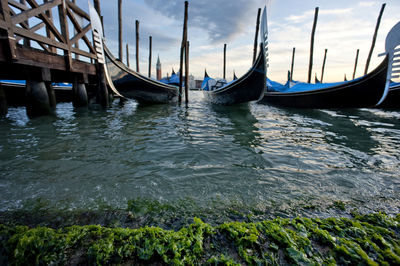 Gondolas moored on grand canal against cloudy sky