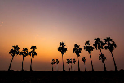 Silhouette palm trees on field against romantic sky at sunset