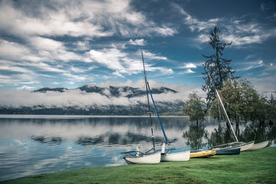 Boats by calm lake against cloudy sky