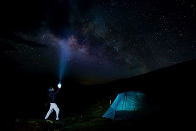 Side view of man with illuminated flashlight against star field at night