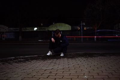 Full length of man sitting on footpath in city