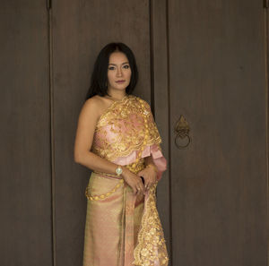 Portrait of young woman wearing traditional clothing standing against cabinet 