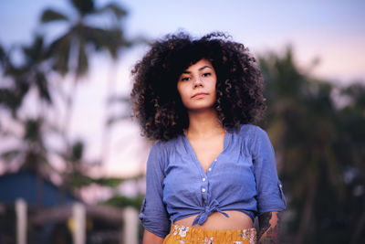 Portrait of young woman with curly hair standing against trees