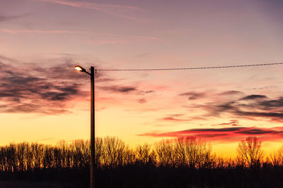 Silhouette trees and electricity pylon against sky during sunset