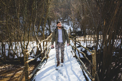 Man crossing footbridge over river in forest during winter