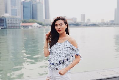 Portrait of young woman standing against river in city