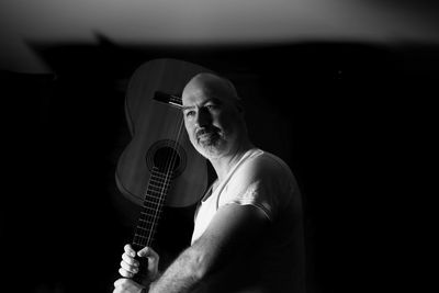 Bald man holding guitar against black background
