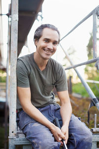 Portrait of smiling man sitting on scaffolding