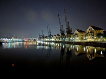 Illuminated buildings by lake against sky at night