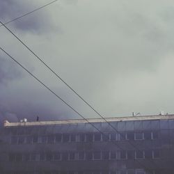 Low angle view of power lines against cloudy sky