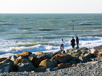 People standing on rocks while looking at sea