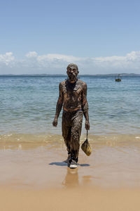 Man covered in oil walking on the sandy beach with the sea in the background.