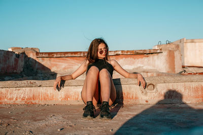 Full length of young woman sitting on wall against clear sky