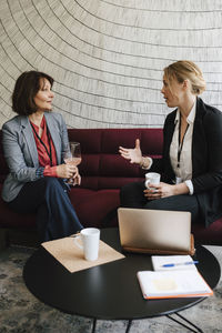 Businesswoman gesturing while discussing with female professional on sofa at convention center