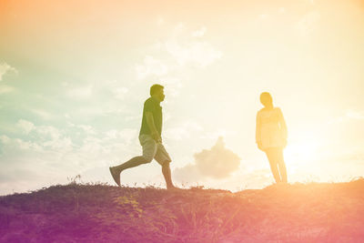 Rear view of people on field against sky during sunset