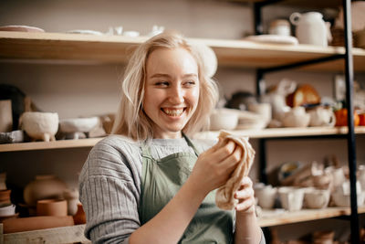 Smiling female potter in the workshop against rack of pottery