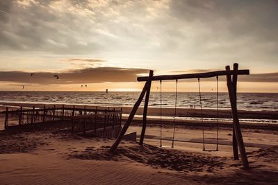 Swings at beach against sky during sunset