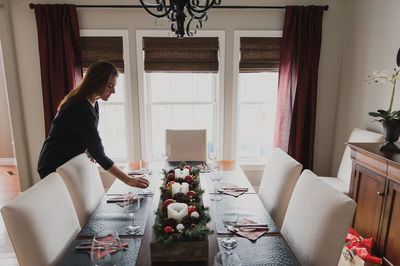 Woman placing a glass on a dining table set for a holiday dinner.