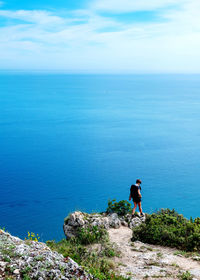 Rear view of man standing on cliff by sea against sky