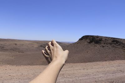 Midsection of person on arid landscape against clear sky