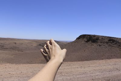 Cropped hand on arid landscape against clear sky