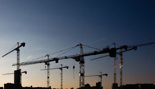 Silhouette cranes against sky at sunset