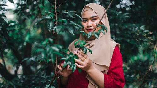 Portrait of young woman standing against plants