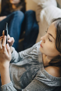 Girl using mobile phone while resting with friend on sofa at home