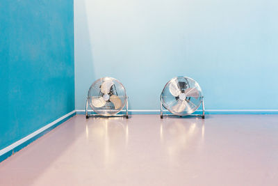 Electric fans on floor against blue wall