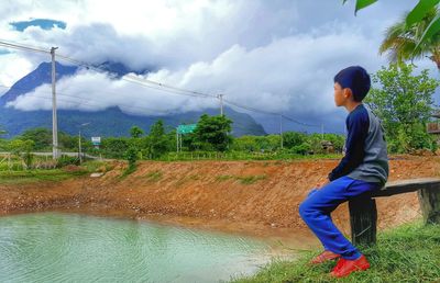 Full length of boy splashing water against cloudy sky
