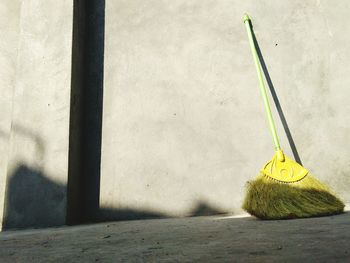 Broom on footpath against concrete wall during sunny day