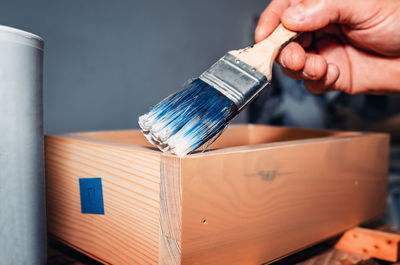 A handyman applies varnish with a brush to a wooden drawer for furniture