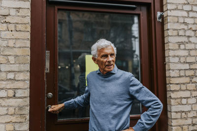 Elderly male entrepreneur standing by door of store