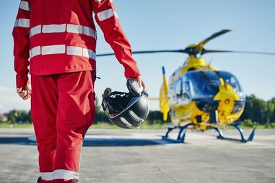 Midsection of rescue worker holding helmet while standing near helicopter at runway