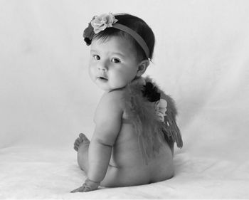 Portrait of cute baby girl sitting on bed against white background