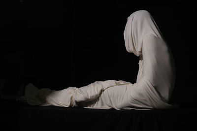 Person wrapped in fabric while sitting against black background